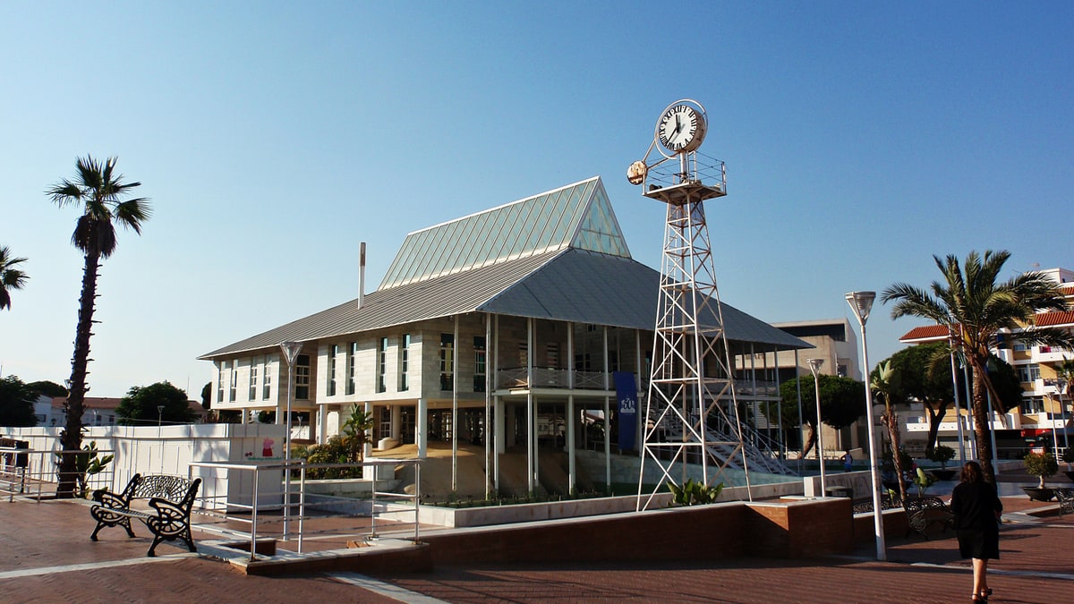 Edificio del Ayuntamiento de Punta Umbría con torre del reloj y palmeras en la plaza.