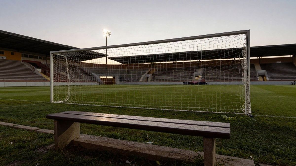 Imagen ilustrativa: un campo de fútbol local al atardecer con la portería y un banquillo vacío en primer plano