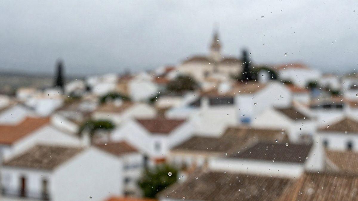 Imagen ilustrativa: gotas de lluvia sobre el cristal de una ventana con un pueblo blanco andaluz desenfocado al fondo
