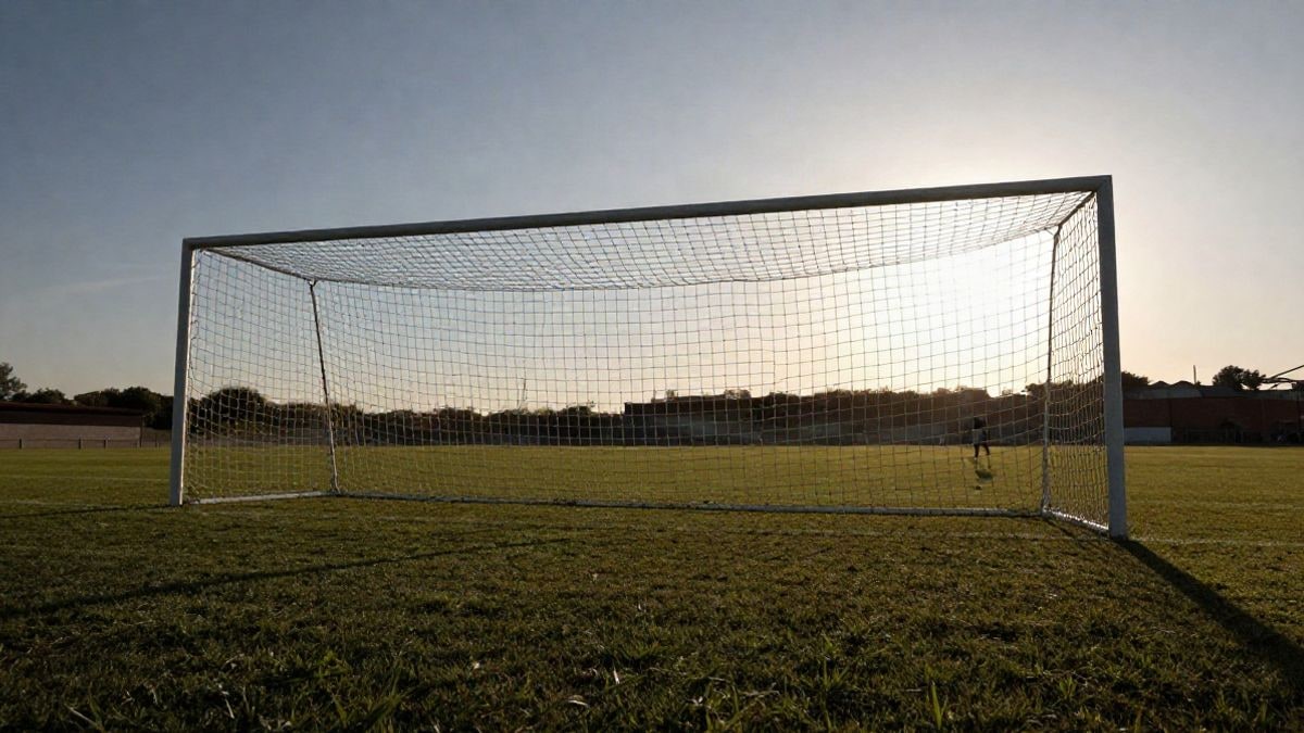 Imagen ilustrativa: campo de fútbol al atardecer con la portería vacía y un jugador alejándose al fondo