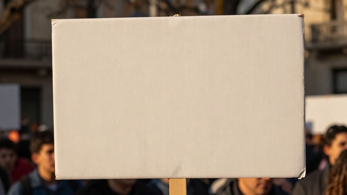 Imagen ilustrativa: primer plano de un cartel de protesta sostenido por una multitud desenfocada en una plaza