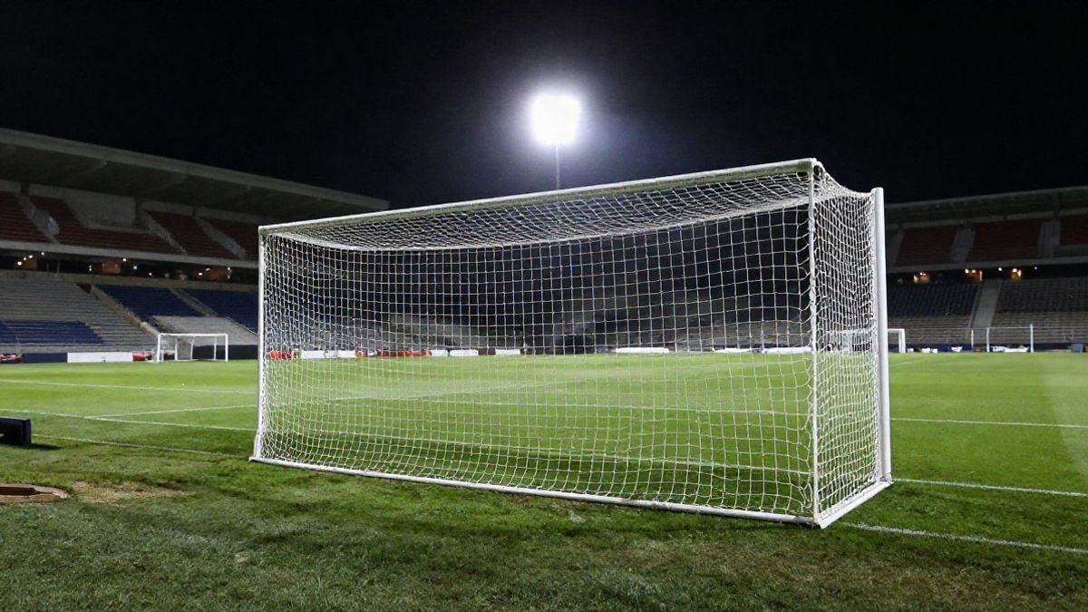 Imagen ilustrativa: estadio de fútbol iluminado de noche con el césped vacío y la portería a contraluz