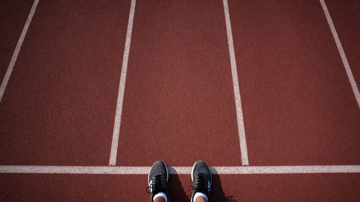 Imagen ilustrativa: vista cenital de una pista de atletismo con zapatillas en la línea de salida
