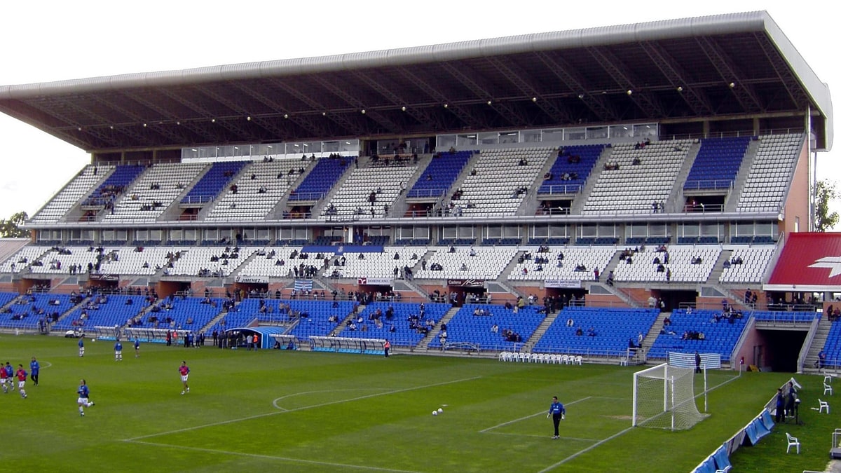 Jugadores calentando sobre el césped del Nuevo Colombino en Huelva, con la grada vacía al fondo.