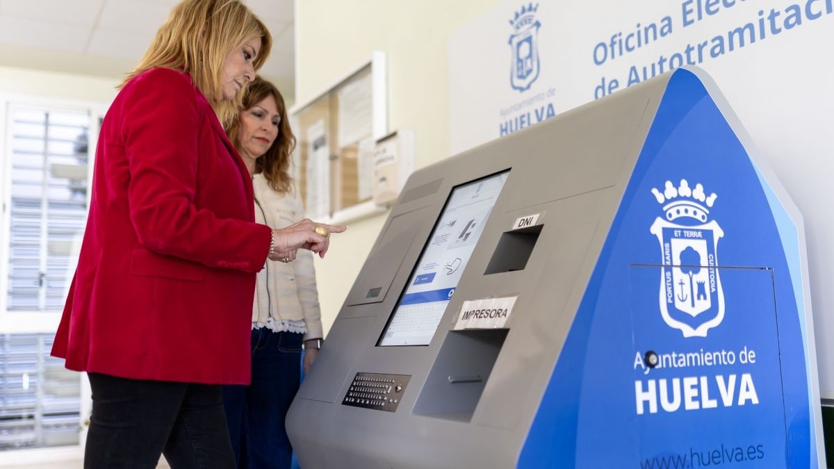 Imagen ilustrativa: una oficina municipal moderna con un quiosco digital de autotramitación y una persona de espaldas usándolo.