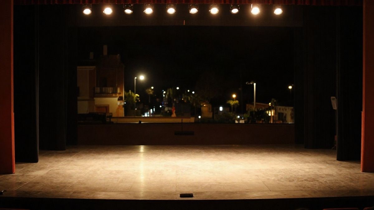 Imagen ilustrativa: un escenario vacío iluminado por focos cálidos en un teatro de noche
