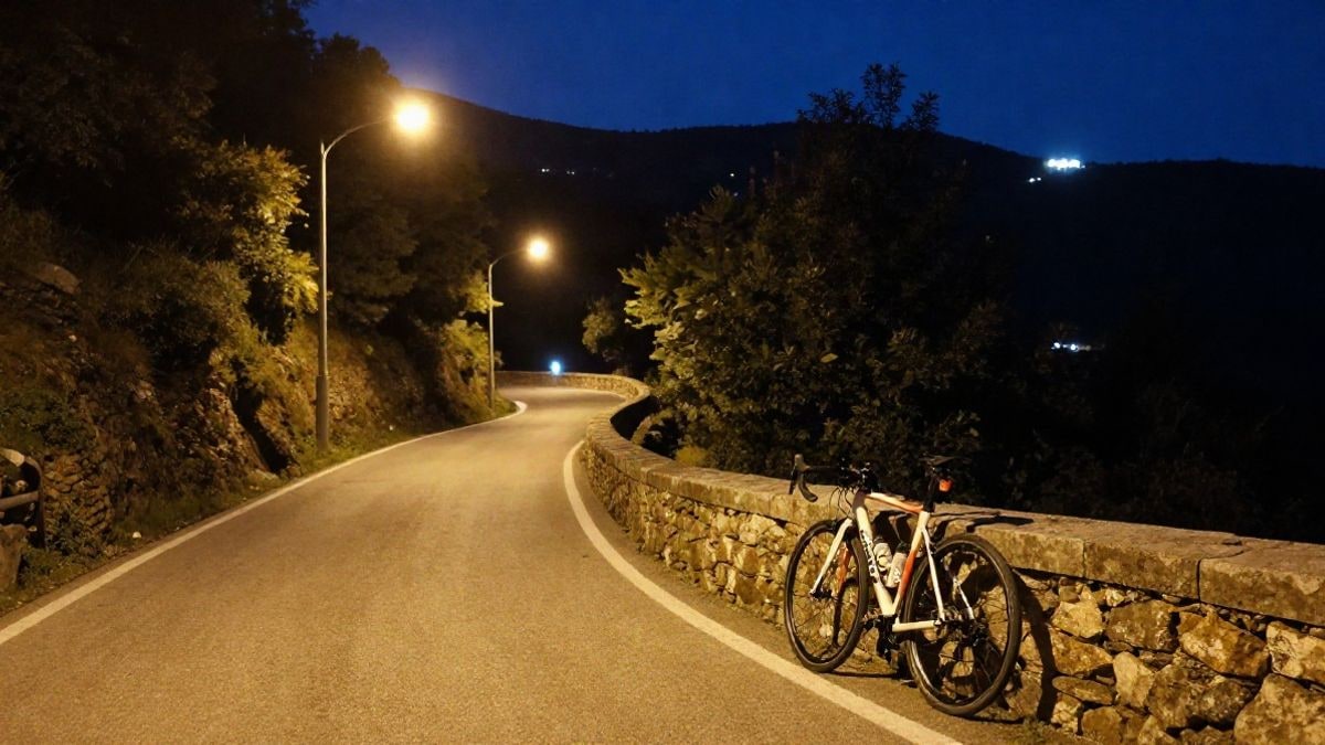 Imagen ilustrativa: una carretera de montaña iluminada por farolas al anochecer con una bicicleta apoyada en un muro de piedra