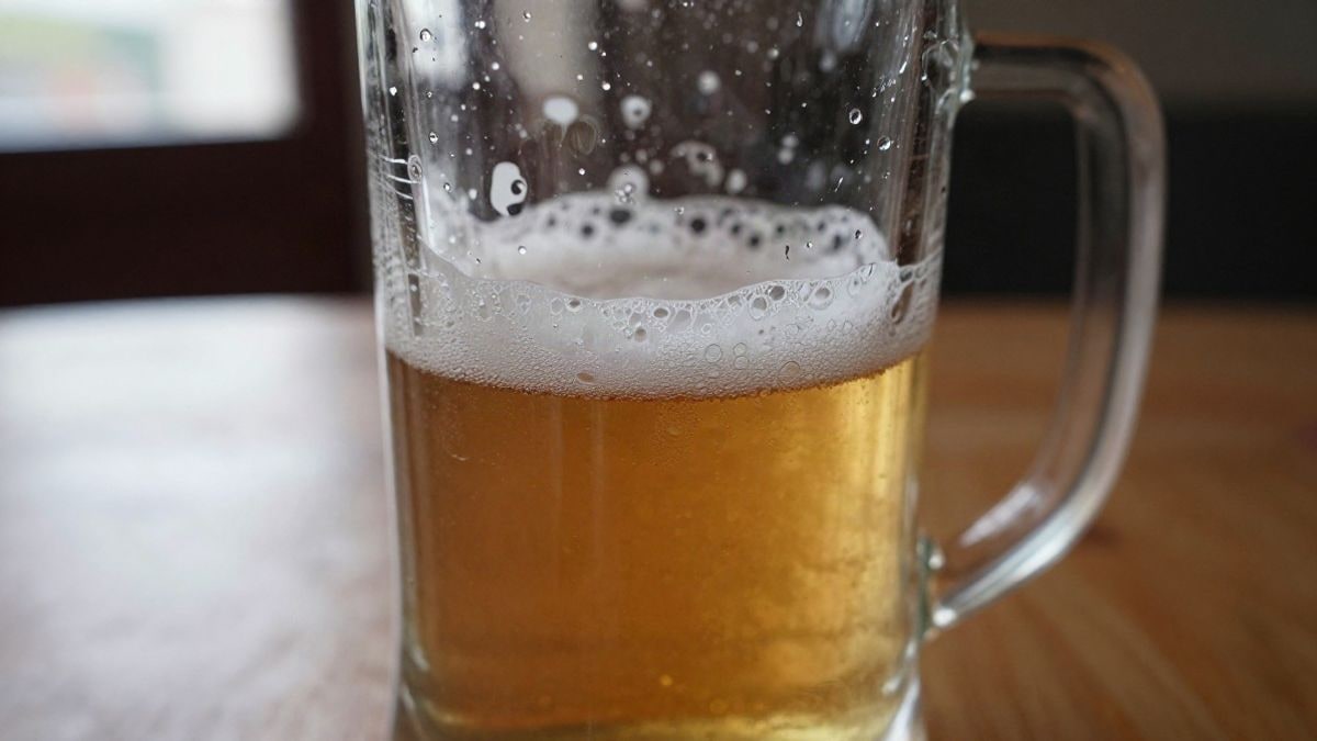 Imagen ilustrativa: primer plano de una jarra de cerveza con espuma sobre una mesa de madera