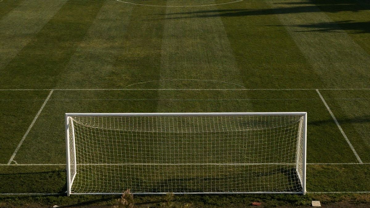 Imagen ilustrativa: vista cenital de un campo de fútbol con líneas blancas y portería al atardecer