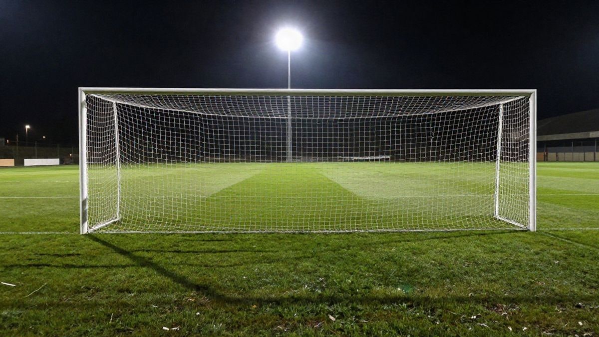 Imagen ilustrativa: portería de fútbol con red bajo focos nocturnos en un estadio vacío