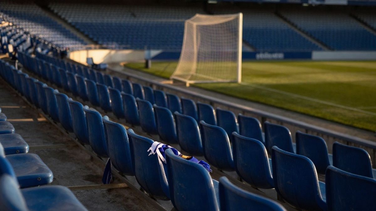 Imagen ilustrativa: gradas vacías de un estadio de fútbol con luz de atardecer y una bufanda sobre un asiento