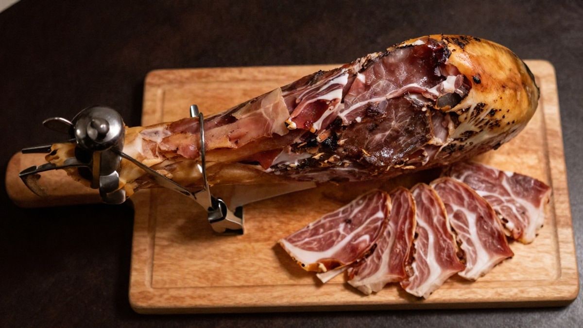 Imagen ilustrativa: vista cenital de un jamón ibérico sobre tabla de madera con cuchillos y lonchas cortadas
