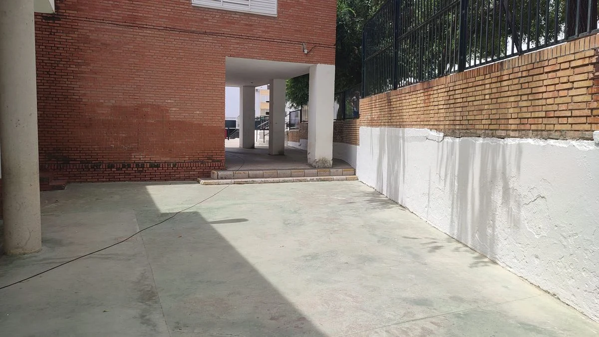 Imagen ilustrativa: fachada de un colegio al atardecer con un operario pintando la pared, iluminada por farolas.