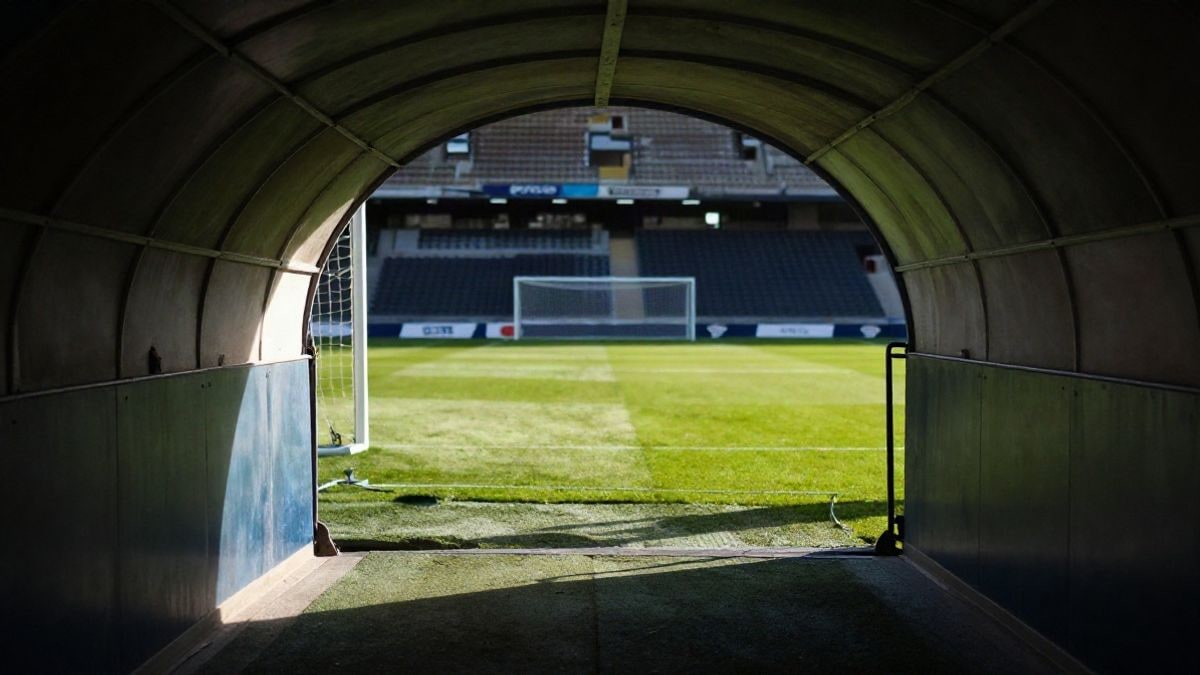 Imagen ilustrativa: túnel de vestuarios que conduce al césped de un estadio de fútbol con la luz de la tarde entrando desde un lateral