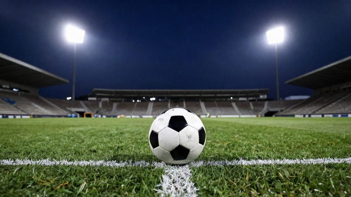Imagen ilustrativa: un balón de fútbol en el punto central de un campo de césped bajo los focos de un estadio por la noche.