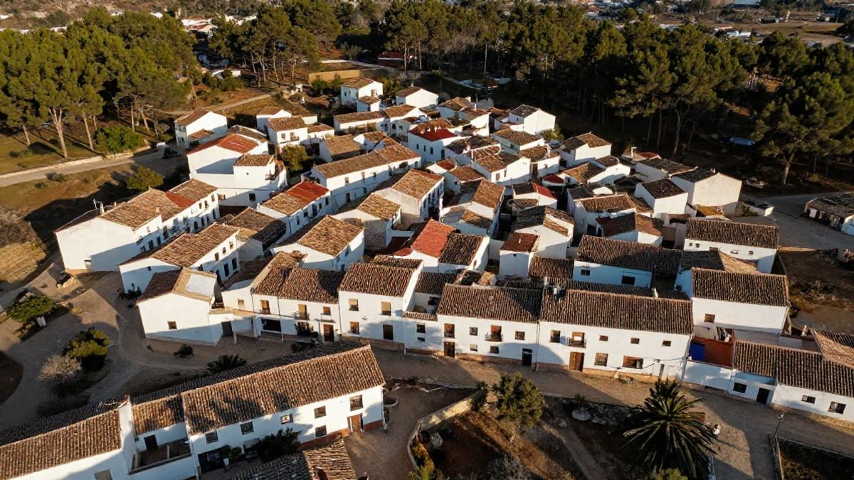 Imagen ilustrativa: vista cenital de un pueblo blanco de calles arenosas rodeado de pinos al atardecer