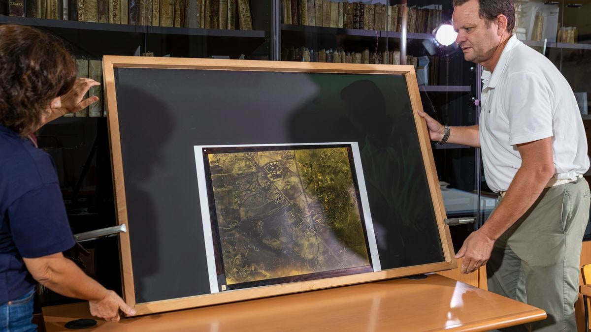 Imagen ilustrativa: mapa antiguo sobre una mesa de madera en un archivo histórico junto a una lupa y guantes blancos