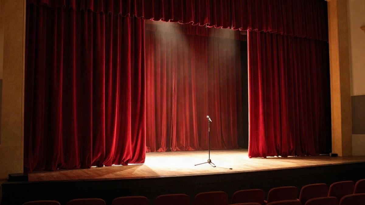 Imagen ilustrativa: escenario de teatro iluminado con cortinas rojas y butacas vacías al atardecer