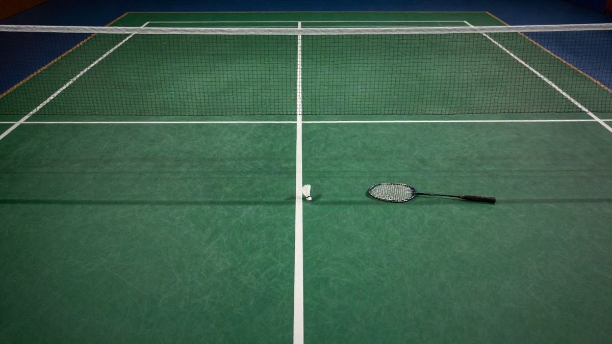 Imagen ilustrativa: vista cenital de una pista de bádminton con la red y un volante en el suelo