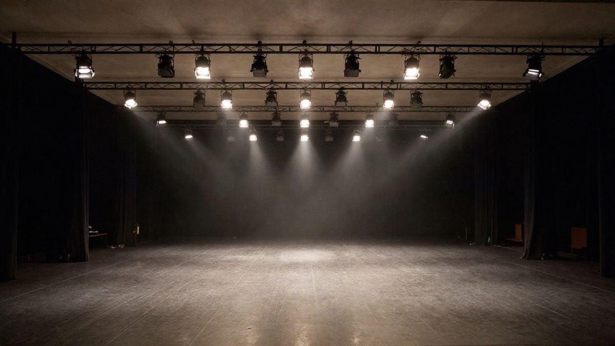 Imagen ilustrativa: escenario vacío de un teatro con focos y líneas que convergen hacia el fondo