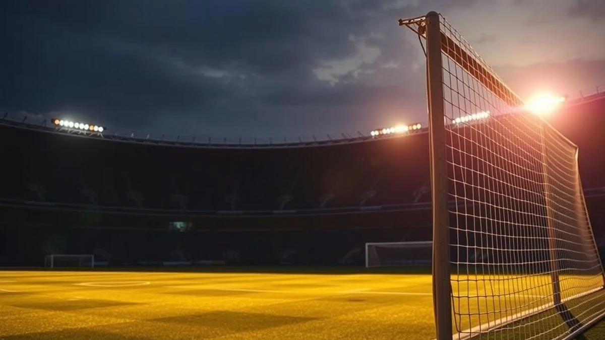 Estadio de fútbol al atardecer con portería y sombras largas en el césped