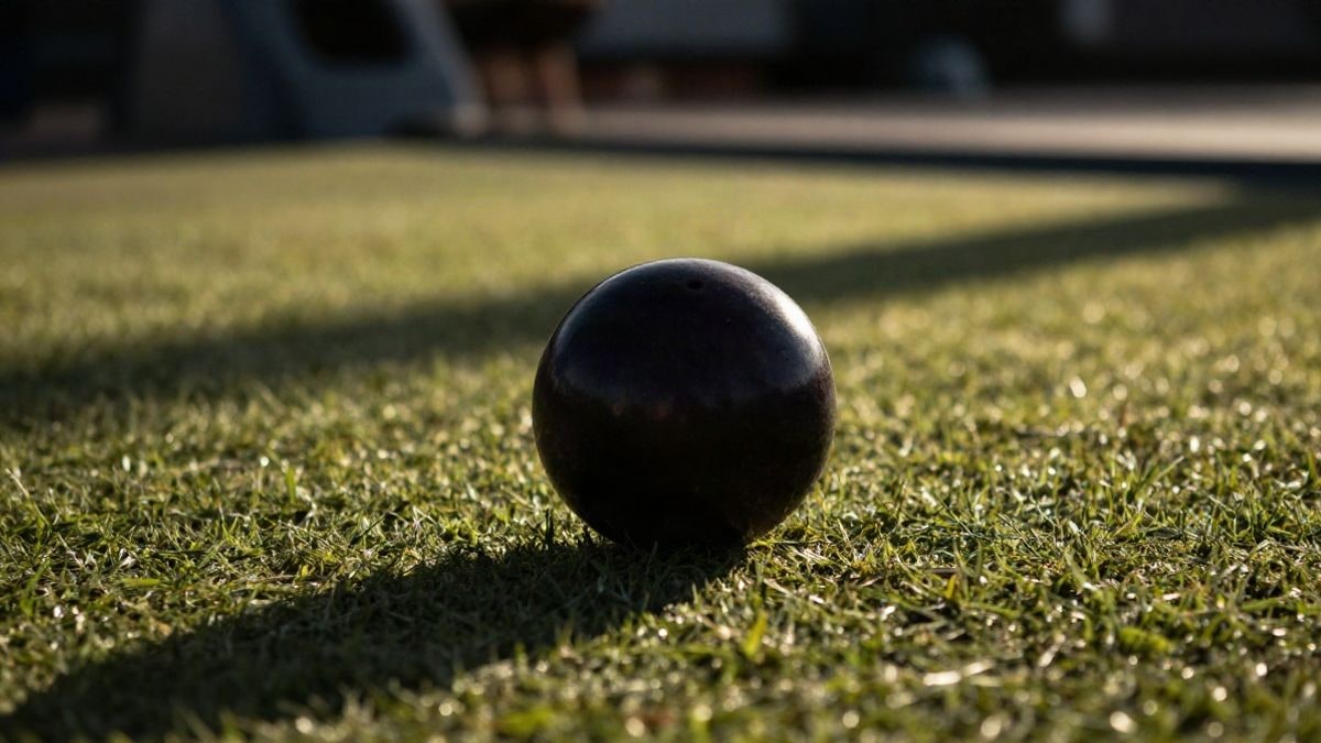 Imagen ilustrativa: detalle de una bola de bowls sobre el césped de un green con luz de atardecer