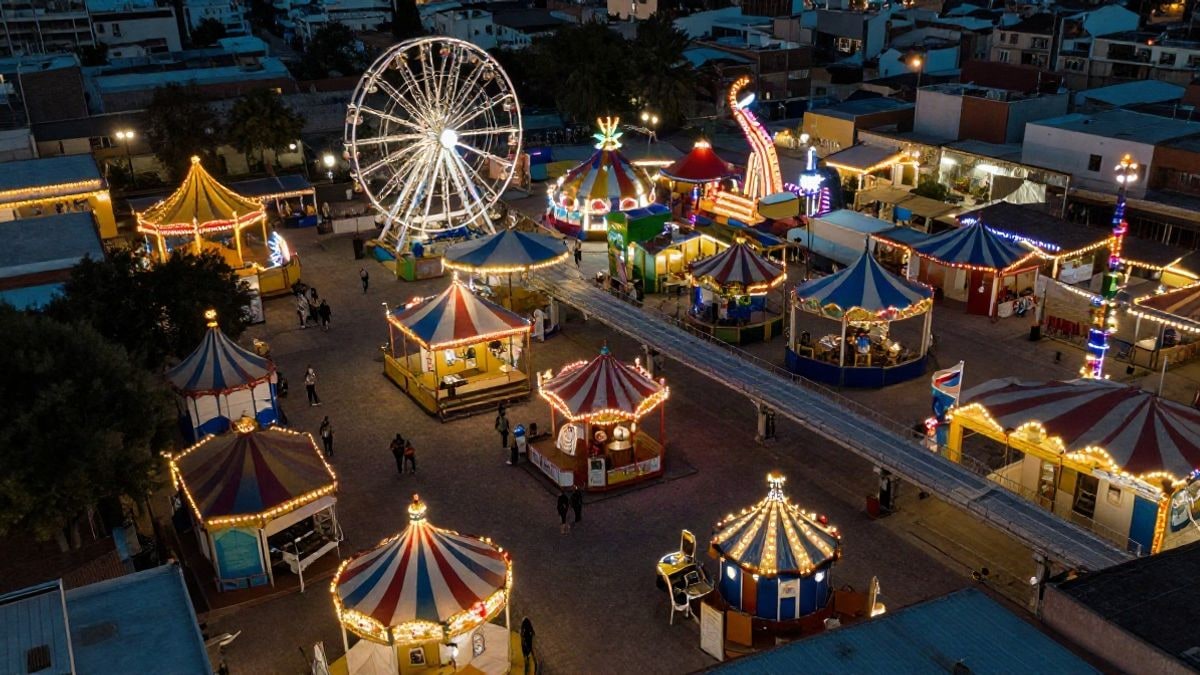 Imagen ilustrativa: vista cenital de un recinto ferial con luces y atracciones al atardecer