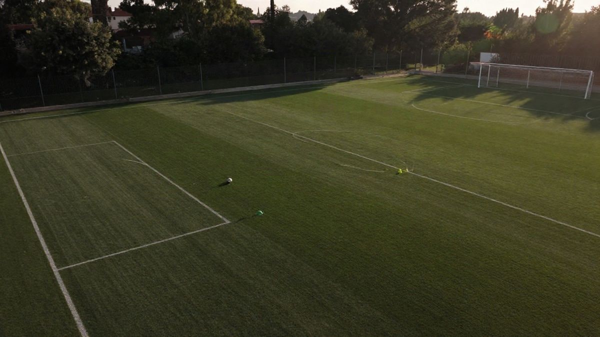 Imagen ilustrativa: vista cenital de un campo de entrenamiento de fútbol con conos y un balón, sin personas
