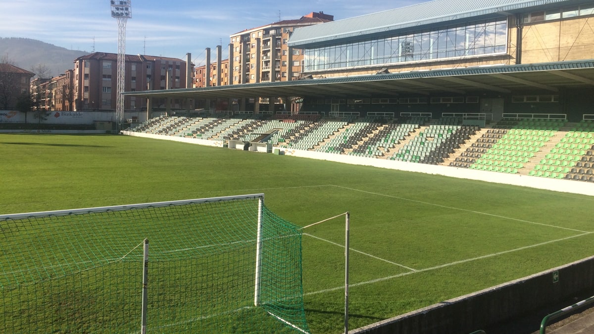 Campo de Las Llanas de Sestao con césped verde, gradas vacías y tribuna cubierta a plena luz