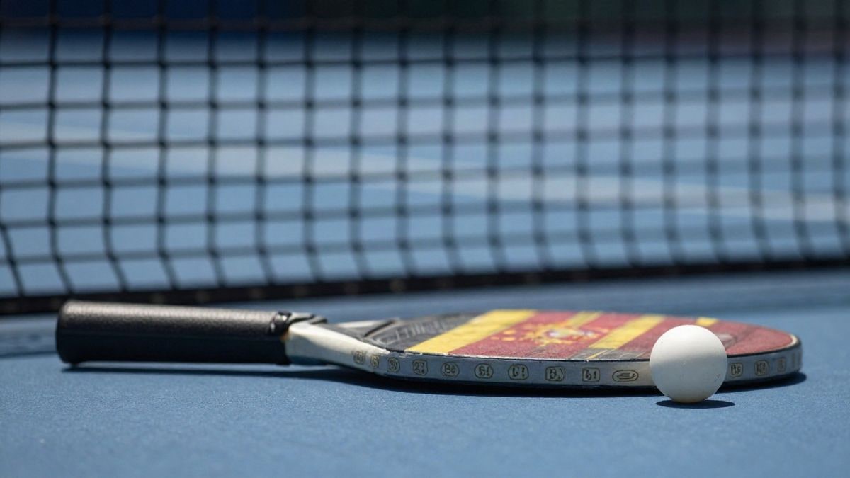 Imagen ilustrativa: pala y pelota de tenis de mesa sobre una mesa azul con la red desenfocada al fondo