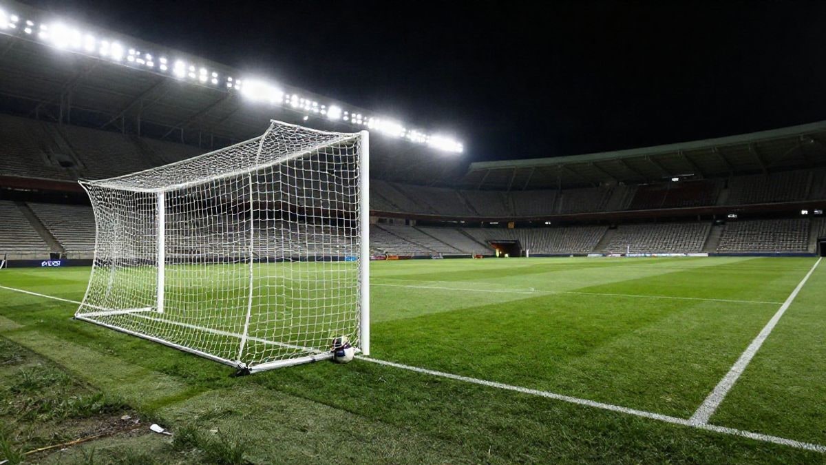 Imagen ilustrativa: estadio de fútbol de noche con focos iluminando el campo y un balón en la red