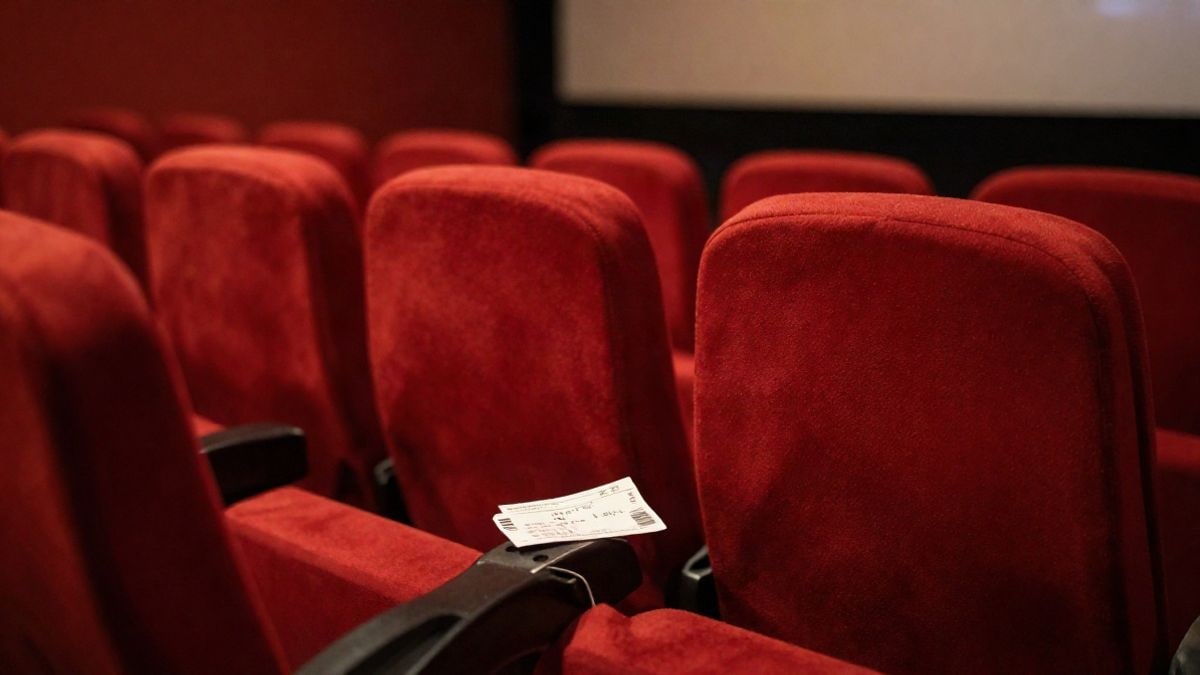 Imagen ilustrativa: fila de butacas rojas vacías en una sala de cine en penumbra, con un billete sobre un reposabrazos
