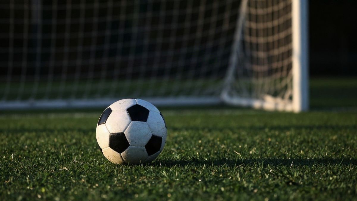 Imagen ilustrativa: un balón de fútbol sobre el césped junto a una portería con la red, al atardecer