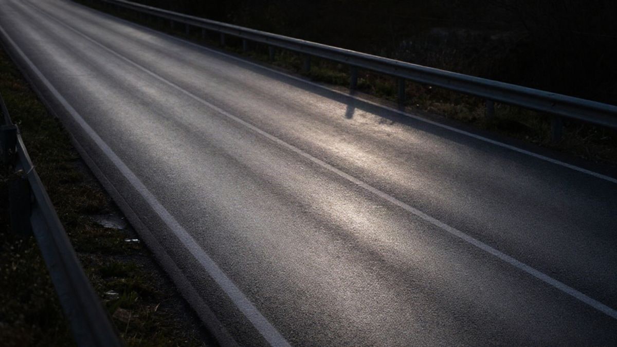 Imagen ilustrativa: una carretera asfaltada y mojada vista desde arriba al atardecer, con quitamiedos y marcas de frenada