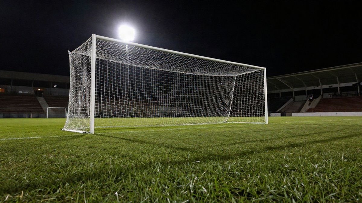 Imagen ilustrativa: portería de fútbol con la red a contraluz bajo los focos de un estadio nocturno