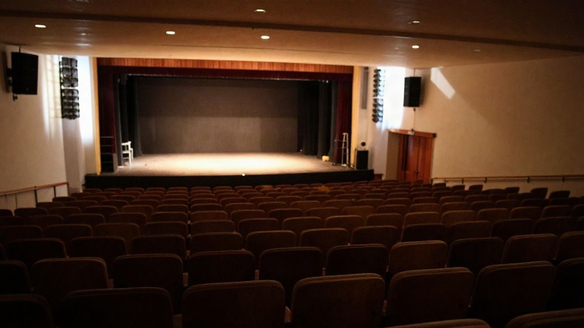 Imagen ilustrativa: filas de butacas vacías de un teatro con un escenario iluminado al fondo