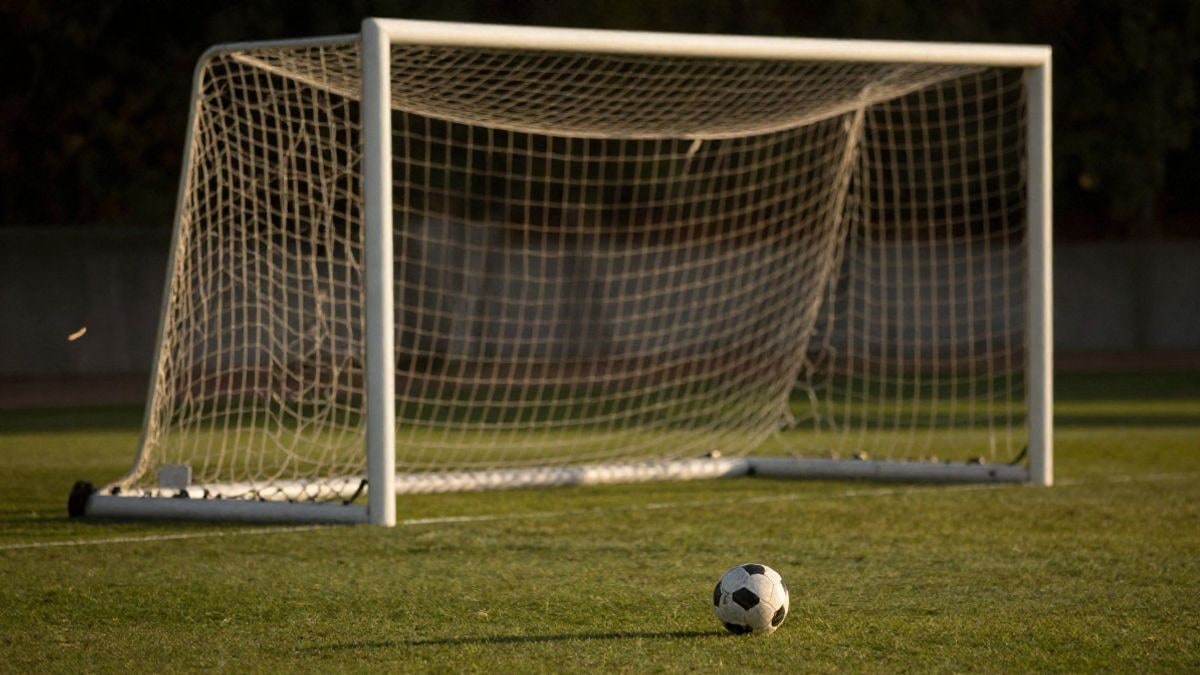 Imagen ilustrativa: portería de fútbol con la red iluminada por luz cálida de atardecer y un balón sobre la hierba