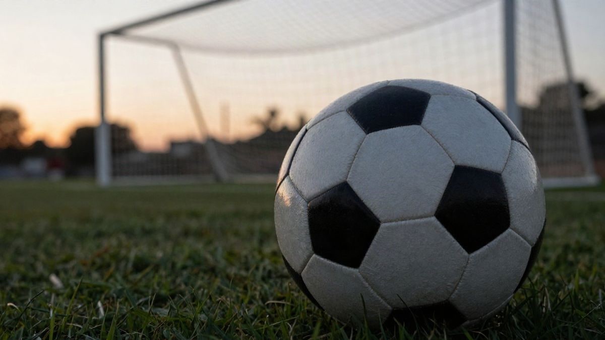 Imagen ilustrativa: primer plano de un balón de fútbol sobre el césped con una portería desenfocada al fondo