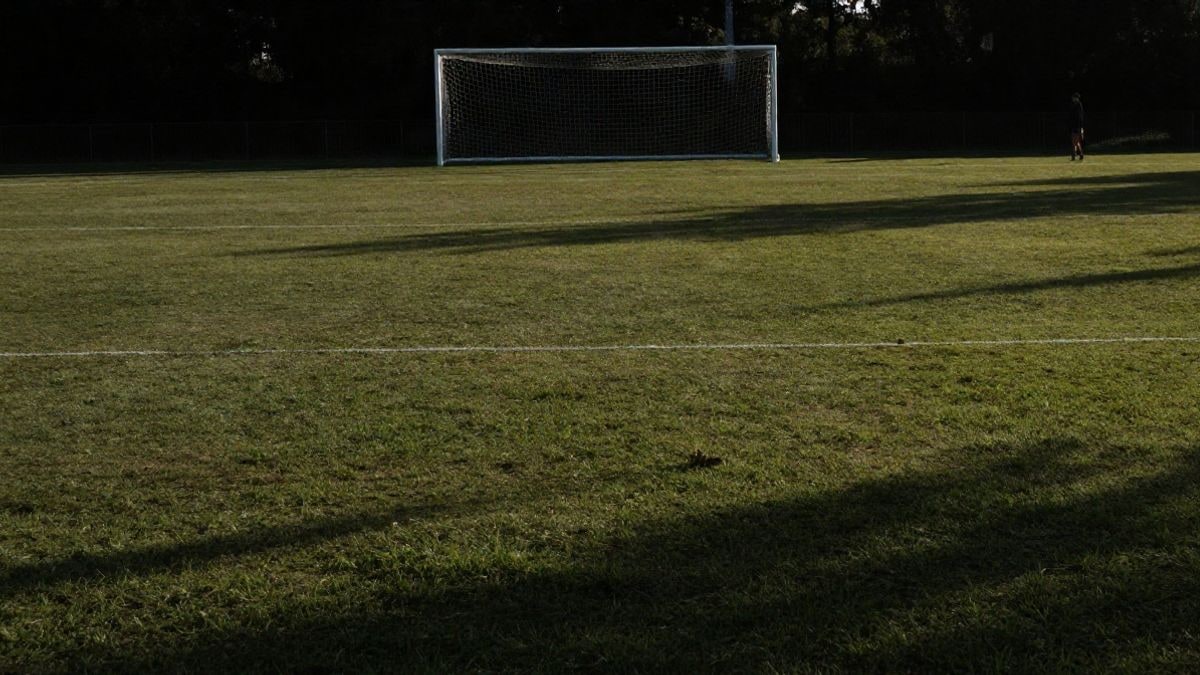 Imagen ilustrativa: campo de fútbol al atardecer con una portería al fondo y una figura lejana
