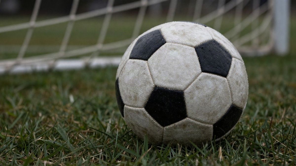 Imagen ilustrativa: detalle de la textura de un balón de fútbol sobre el césped con la red de la portería al fondo