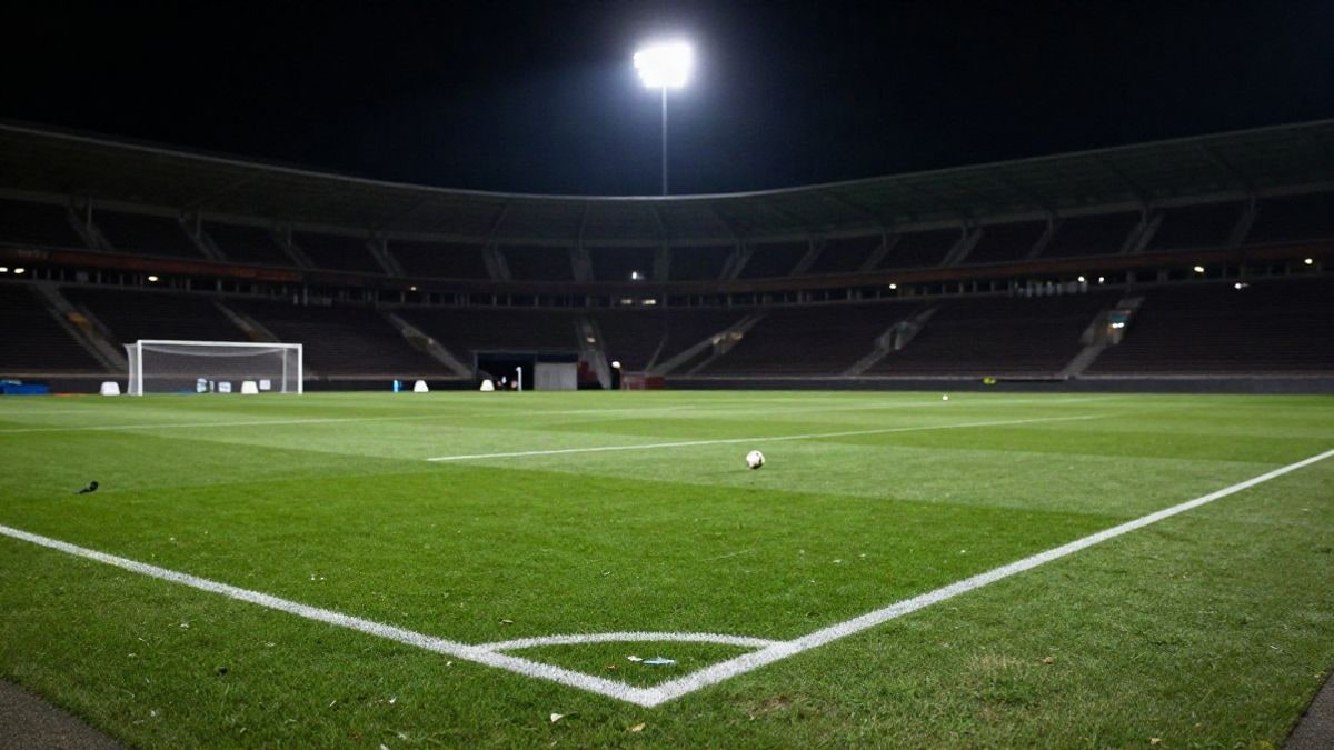 Imagen ilustrativa: estadio de fútbol de noche iluminado por focos, con el césped vacío y un balón en el punto de penalti