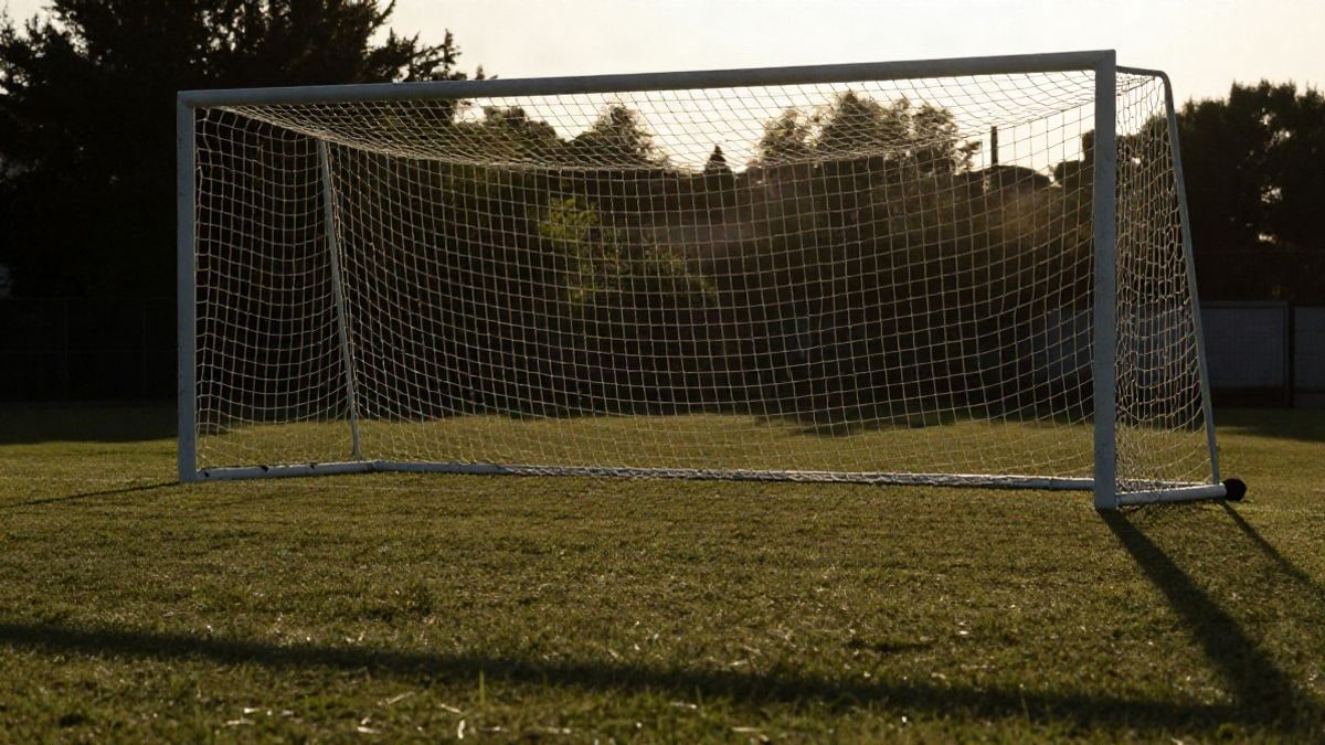 Imagen ilustrativa: una portería de fútbol con la red recortada a contraluz al atardecer y sombras largas sobre la hierba