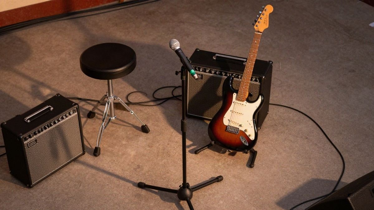 Imagen ilustrativa: vista cenital de un pequeño escenario con micrófono, guitarra eléctrica y taburete de batería