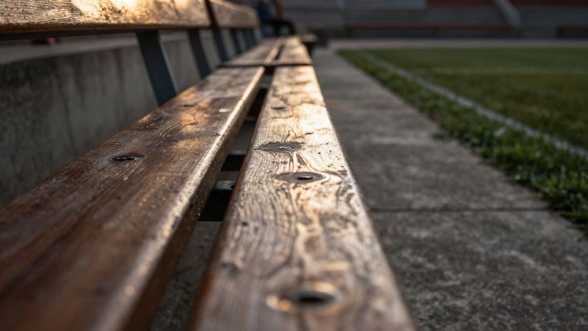 Imagen ilustrativa: detalle de un banco de madera junto a un escalón de hormigón de una grada al atardecer