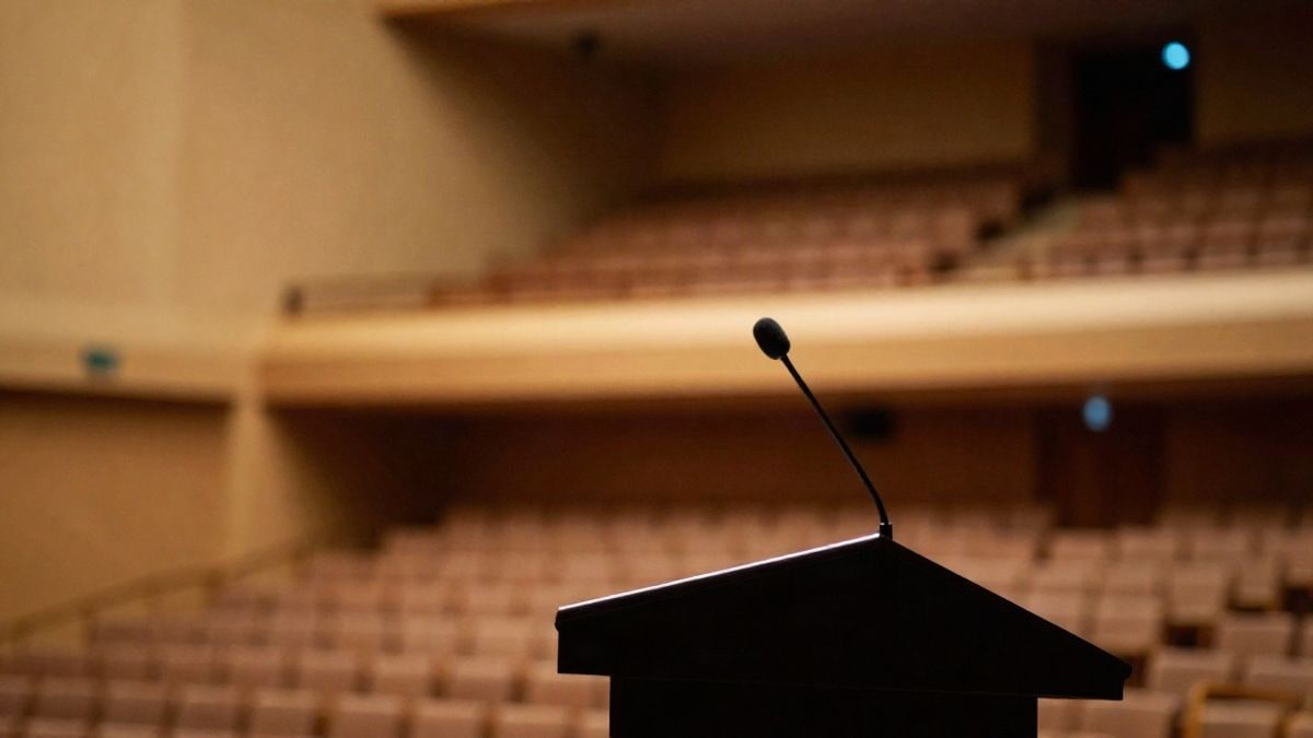 Imagen ilustrativa: atril vacío con micrófono en un auditorio con butacas desenfocadas