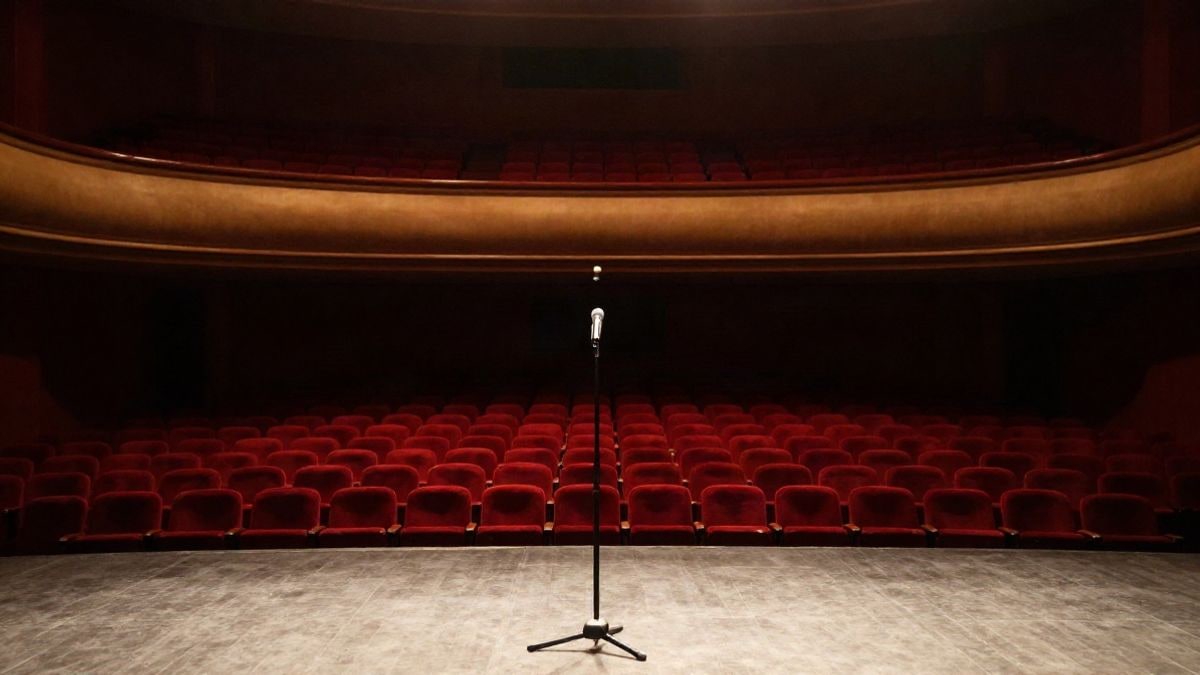 Imagen ilustrativa: escenario vacío de un teatro con un micrófono y butacas al fondo