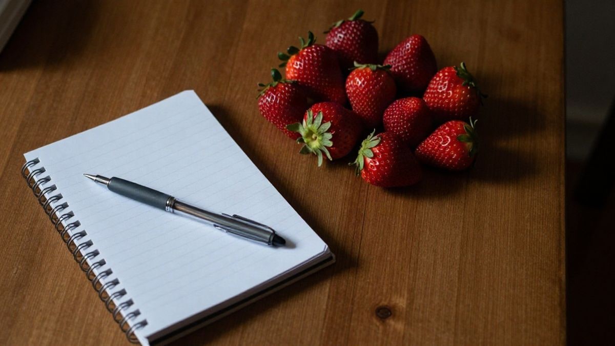 Imagen ilustrativa: vista cenital de una mesa con fresas, un cuaderno y un bolígrafo