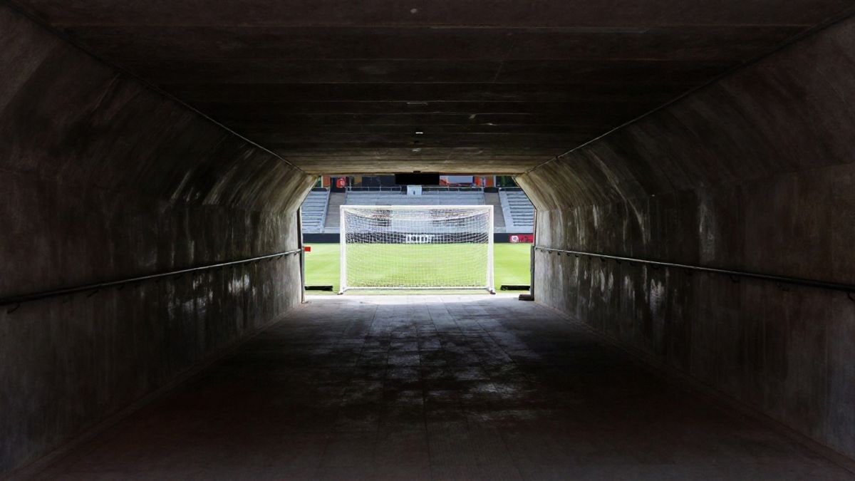 Imagen ilustrativa: túnel de un estadio de fútbol vacío con una portería al fondo iluminada por luz natural