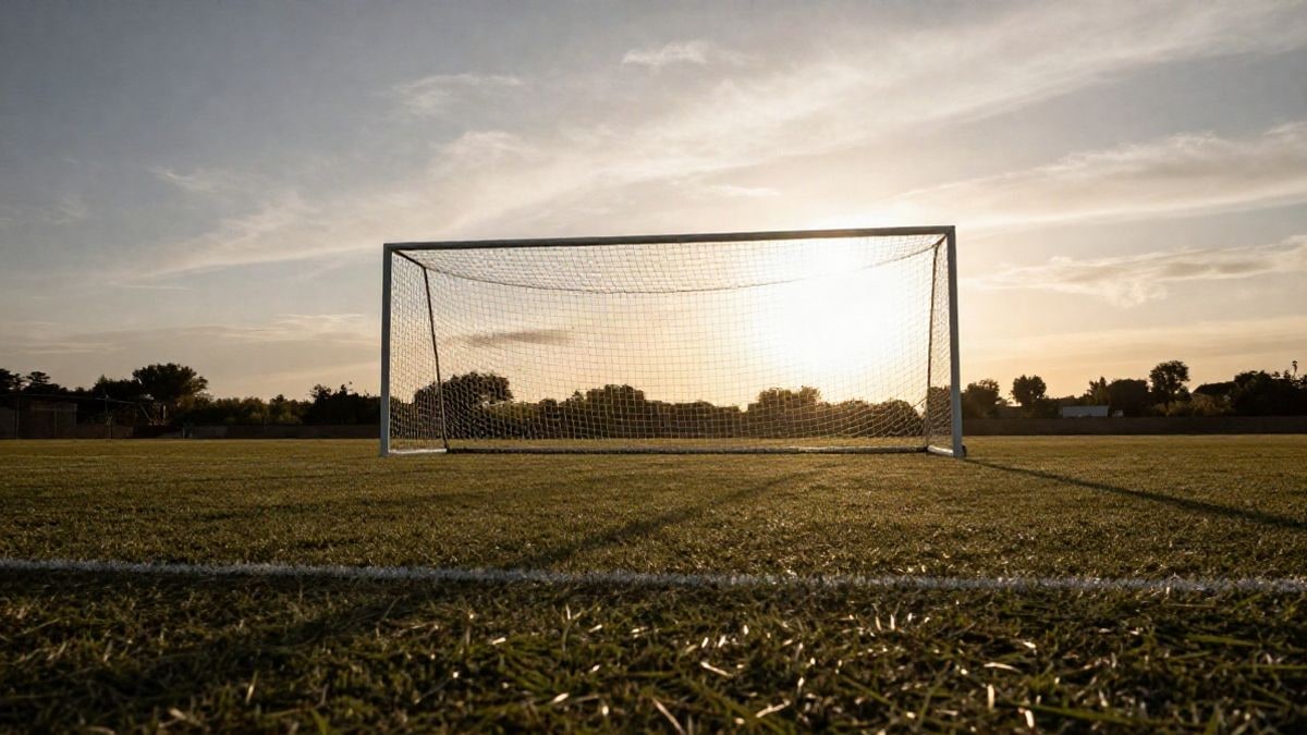 Imagen ilustrativa: ángulo bajo de un campo de fútbol base vacío con la portería recortada contra el cielo al atardecer