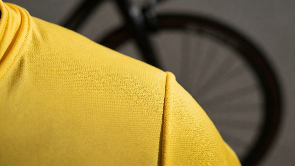 Imagen ilustrativa: textura de maillot amarillo con rueda de bicicleta desenfocada al fondo